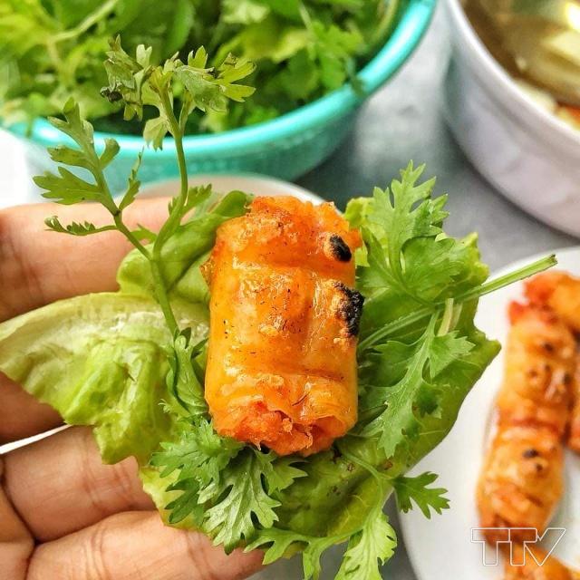 Một miếng chả tôm cuộn với xà lách, cho kèm rau thơm rồi chấm với nước mắm.