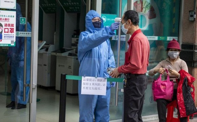 Một nhân viên bảo vệ mặc trang phục phòng dịch đang đo thân nhiệt khách đến giao dịch tại một ngân hàng ở Quảng Châu . Ảnh: EPA.