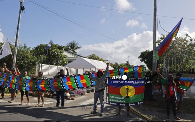 Người dân cầm cờ Kanak biểu tình khi đoàn xe của Tổng thống Pháp đi qua Noumea, New Caledonia, ngày 23/5 (Ảnh: AFP)